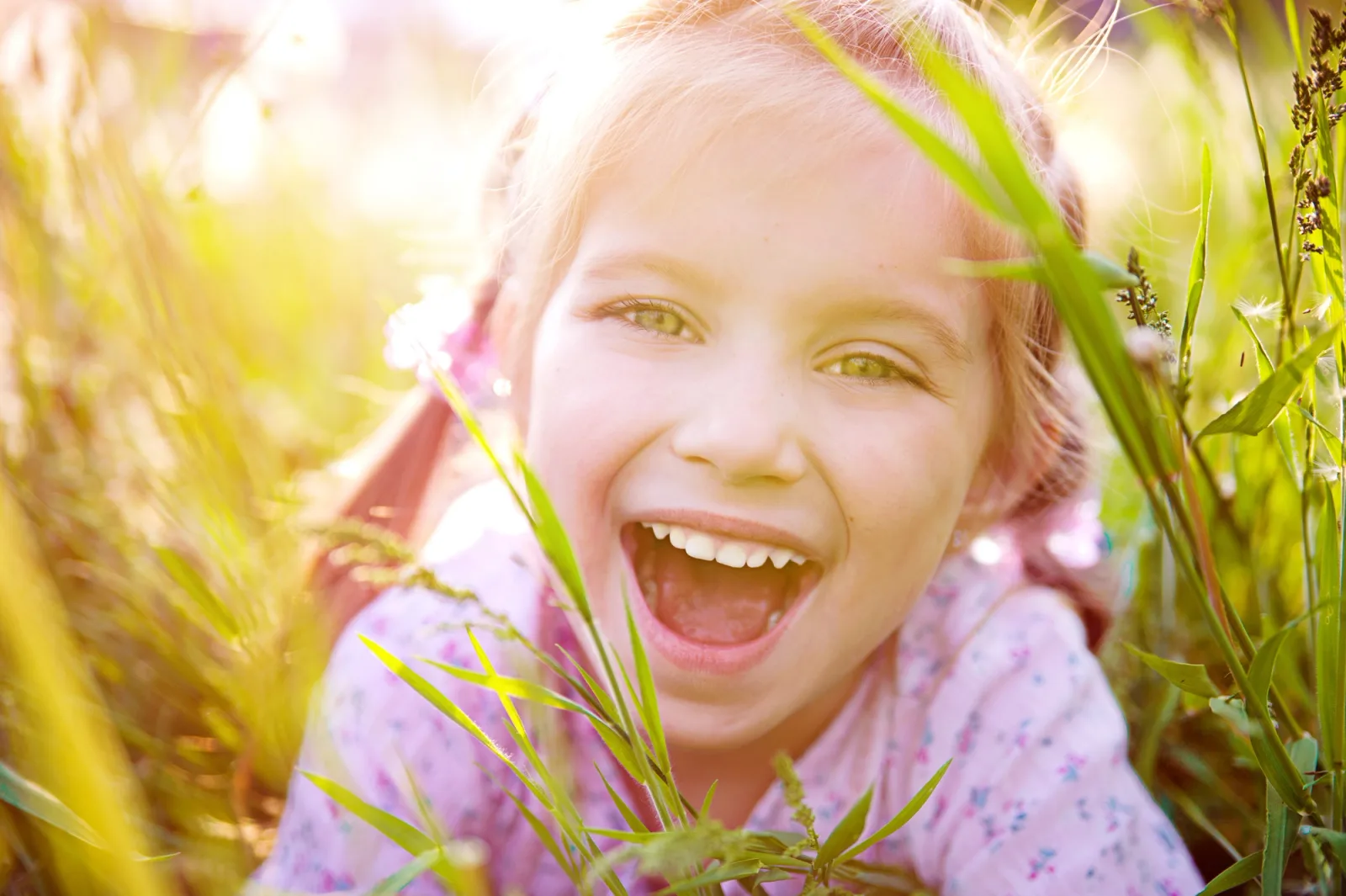 a little girl is laying in the grass with her mouth open .