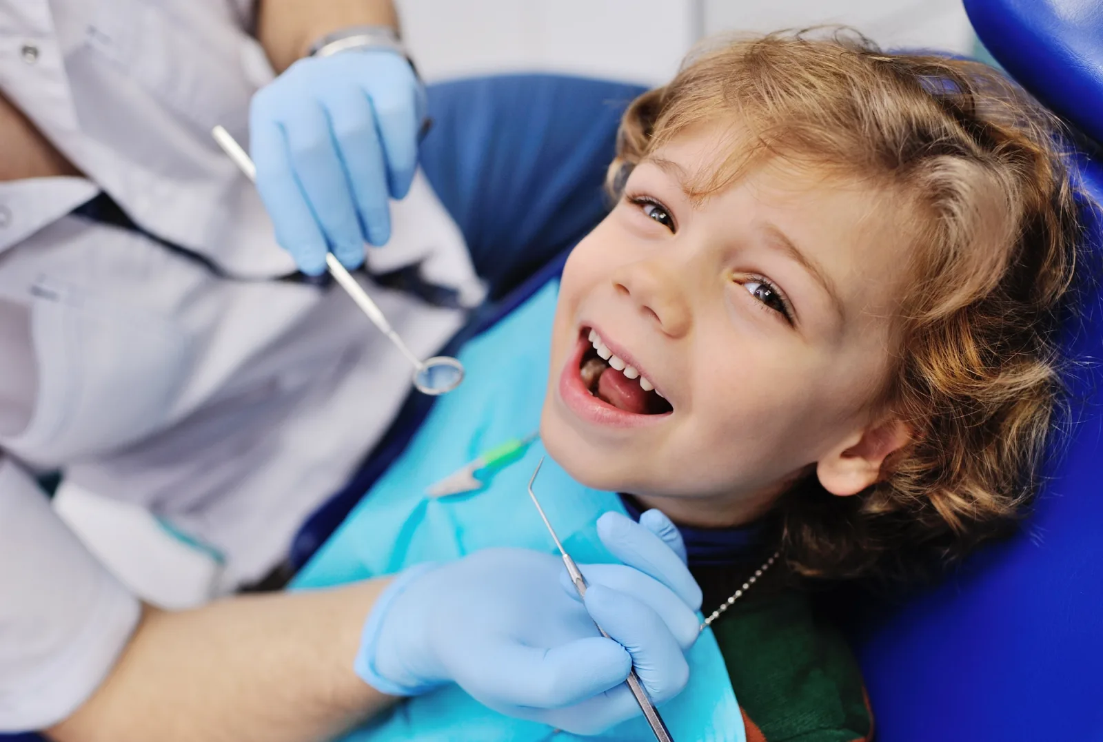 a little boy is sitting in a dental chair while a dentist examines his teeth .