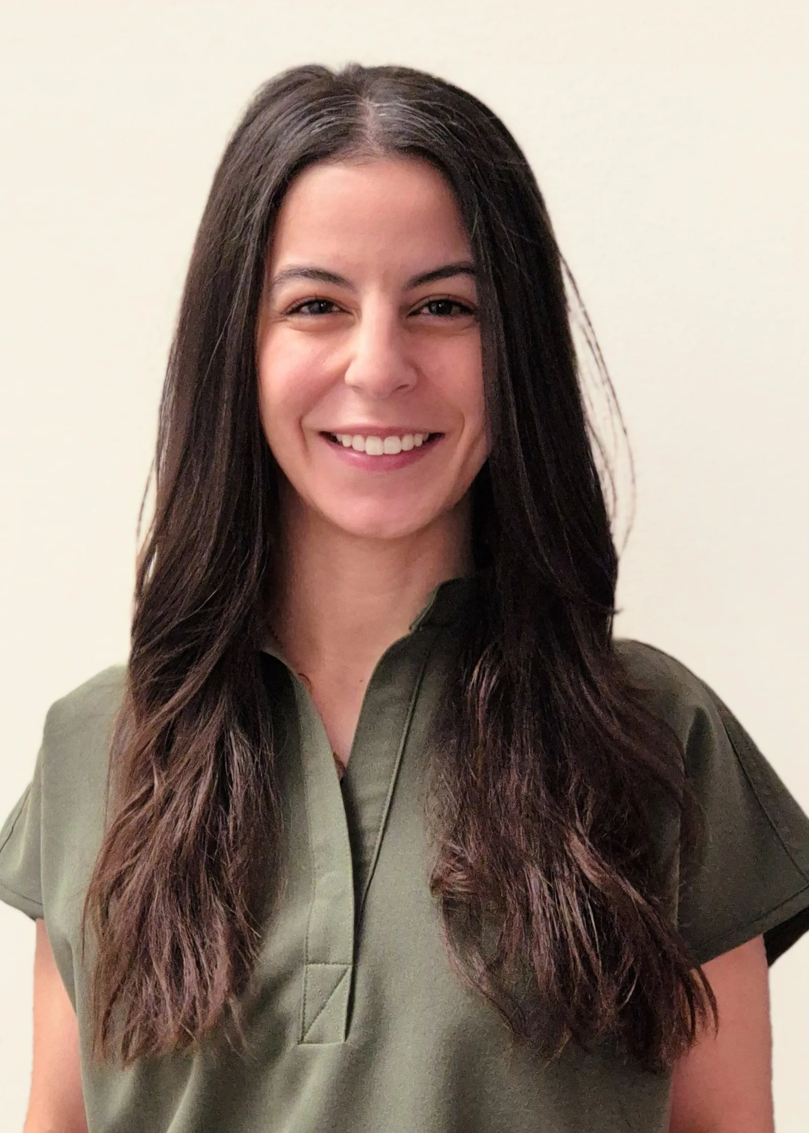 A smiling woman with long dark hair wears a green collared top.