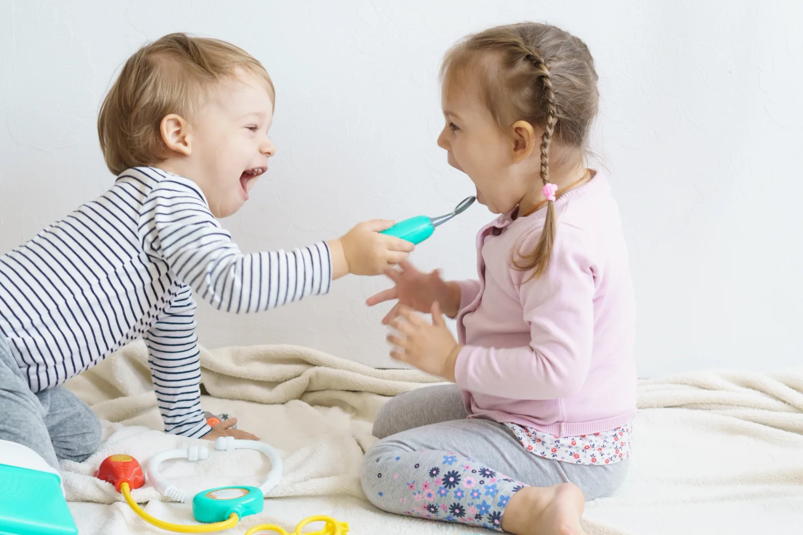 a boy and a girl are playing with toys on a bed .